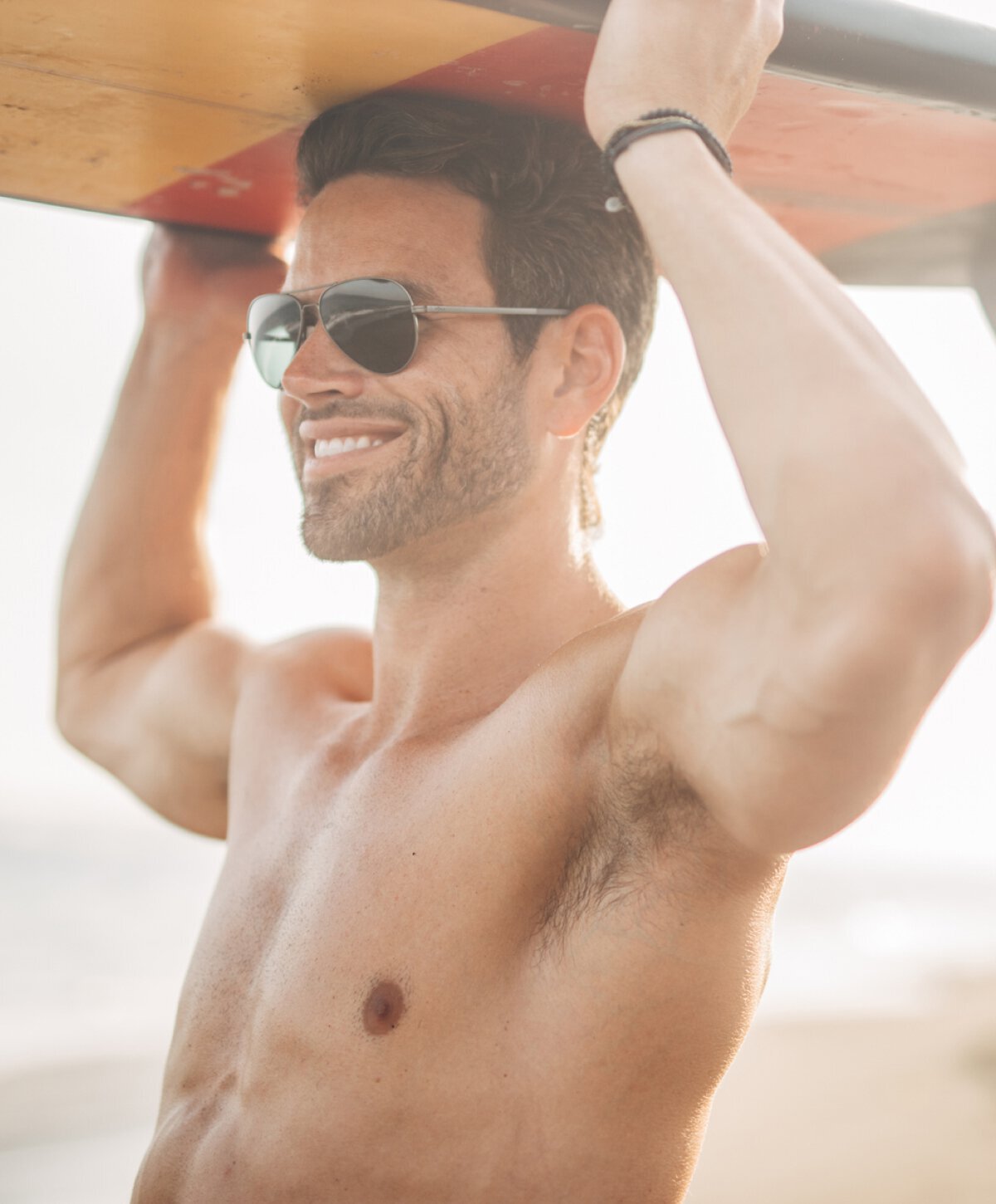 Man after gynecomastia surgery holding a surfboard above his head